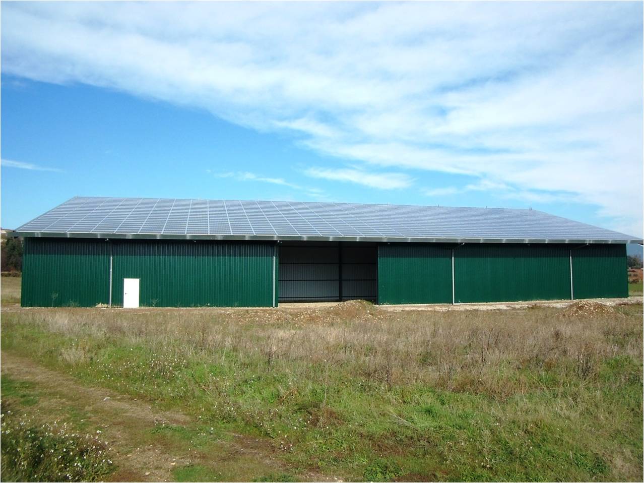 Un bâtiment agricole vert dont le toit est équipé de panneaux photovoltaïques.